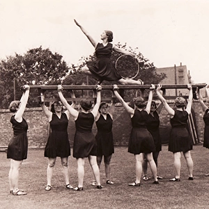 Eight girls hold aloft ninth on gym bench posing with hoop