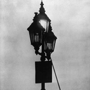 A lamplighter at work in the London fog