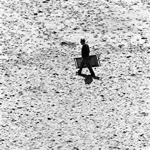 Man walks across Tenby beach carrying a deck chair