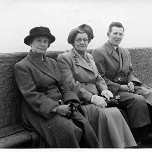 Two mature women with a younger man pose for a snap on a bench along the sea front at an