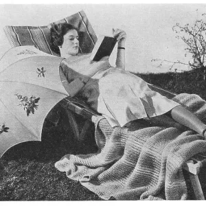 Model reading on a garden lounger with an umbrella, wearing very thick silk stockings, advertising patterns for an embroidered sunshade and knitted blanket. Date: 1935 Model reading on a garden lounger with an umbrella, wearing very thick silk stockings, advertising patterns for an embroidered sunshade and knitted blanket. Date: 1935