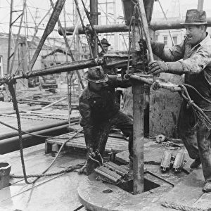 Oil field workers adding a length of pipe to drill stream by