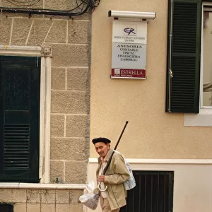 An old man walks down a street in Menorca, Spain