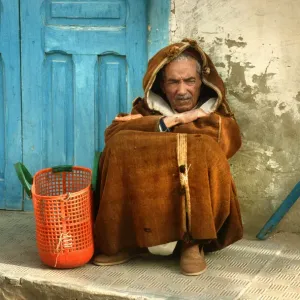 Old man wearing a djelleba sits on pavement, Tunisia Old man wearing a djelleba sits on pavement, Tunisia