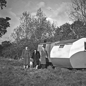 People and dog in a field next to two caravans