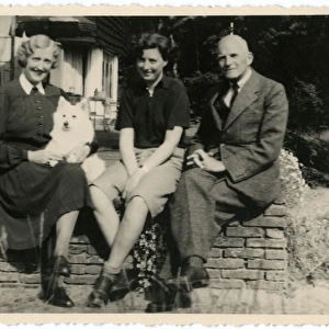 Three people in a garden with a dog