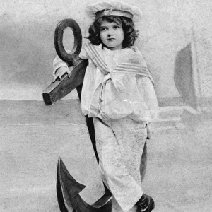 Small boy in a sailor suit poses with a large anchor