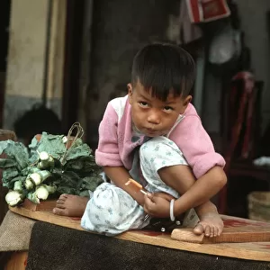 A small boy sits on his mothers vegetable stall, Hong Kong