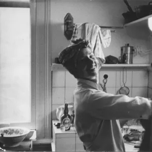 A smiling young woman in a headscarf and apron washing up or preparing food in a kitchen