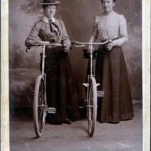 A splendid cabinet photograph of two well-dressed women standing proudly with their bicycles