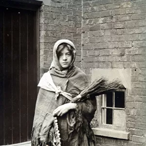 Woman dressed as winter, swaddled in rag and carrying fire wood. Date: c. 1915