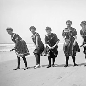 Women on the beach in period bathing costumes wring out wate