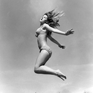 Young woman leaps up from a sand dune, Cornwall