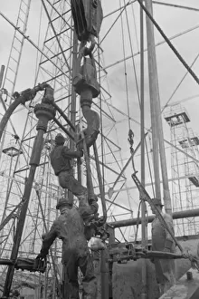 Activity at oil well; man on lengths of traveling block will