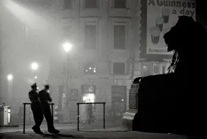 Atmospheric shot of two policement in silhouette resting in Trafalgar Square in front of giant lion statue Date: early 1950s