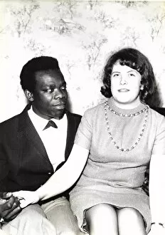 Black man and white woman sitting on a bed holding hands