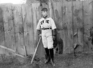 A boy in baseball uniform by a fence in America