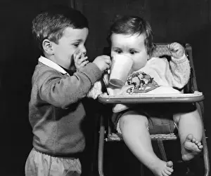 Boy giving drink to a baby in a high chair