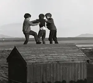 Three boys playing on top of a wooden shed