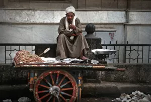 Images Dated 8th August 2019: Cairo street seller sits on his barrow smoking a cigarette