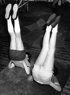 Lesson Prints: Children doing leg exercises on a mat in the school gym. Date: 1960s