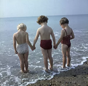 Images Dated 26th May 2017: Three children holding hands, paddling in the sea