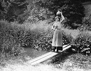 Countrywoman carrying a pot over a bridge, 1890s