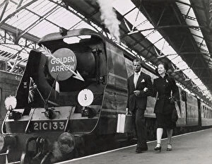 Dover Collection: A couple walk arm in arm on a railway platform, beside the luxury locomotive the Golden Arrow