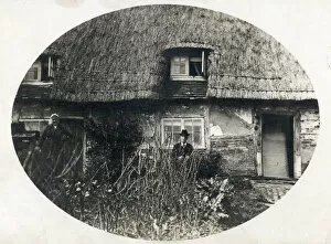Elderly couple standing proudly outside their thatched English country cottage