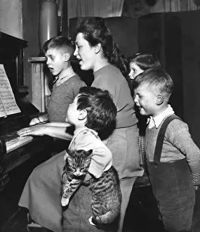 Carols Prints: Family and cat practising Christmas carols at the piano