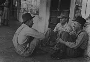 Spur Gallery: Farmers sitting aginst wall and squatting on sidewalk. Spur