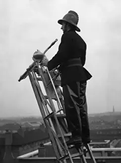 Rooftops Prints: Firefighter using hook belt at top of ladder