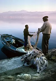 Two fishermen sort their nets on stone quayside - Fetheye