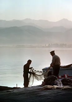 Images Dated 27th August 2019: Two fishermen sort their nets on stone quayside - Fetheye