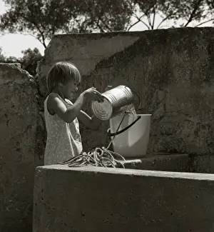 Girl pouring water from a tin into a bucket