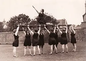 Eight girls hold aloft ninth on gym bench posing with hoop