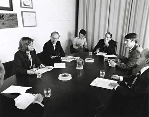 Notes Prints: A group of men and women sit around a table holding a board meeting