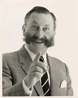 Bushy Prints: Head and shoulders portrait of a smartly dressed man with a bushy moustache pointing