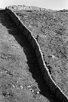 Hiker Prints: Hiker holds on to a stone wall on steep hill, Peak District