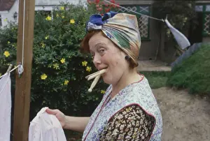 A housewife with a mouthful of clothes pegs strikes a pose as she hangs out the washing! Date: 1940s (re-enactment)