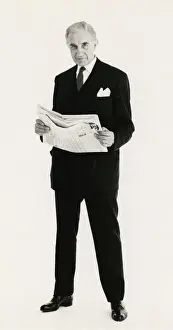 Mature Prints: Full length portrait of a mature man posing in a suit, holding a newspaper