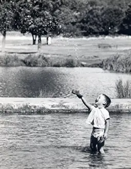 Little boy paddling in a pond holds up his new shoes