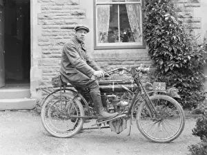 Man on an early motorcycle in front of a house