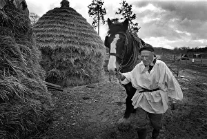 1988 Prints: A man leads a working horse past old-fashioned hay stacks