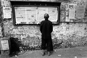 A man readis a newspaper on a noticeboard in a Canton street A man readis a newspaper on a noticeboard in a Canton street