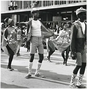 Afro Prints: A man in shorts and long socks dances between two fashionable women at the Port of Spain Carnival