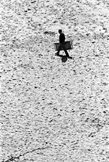 Man walks across Tenby beach carrying a deck chair