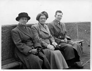 Overcoat Gallery: Two mature women with a younger man pose for a snap on a bench along the sea front at an