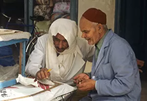 Hooded Collection: Two men sit beside stall in the market at Houmt Souk, Djerba