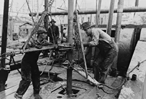 Oil roughnecks screwing one piece of drill pipe to another p